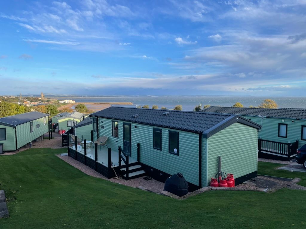 The Cara: a sage-green static caravan with a decked veranda, on a lawn above the bay